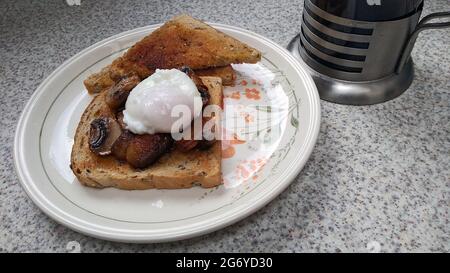 NEWTON le WEIDEN. MERSEYSIDE. ENGLAND. 06-20-21. Ein pochiertes Ei, serviert auf Toast mit Pilzen, zusammen mit einem Kaffeehaus gemahlenem Kaffee. Stockfoto