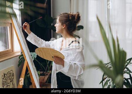 Seitenansicht einer jungen Frau auf Leinwand mit Pinsel Stockfoto