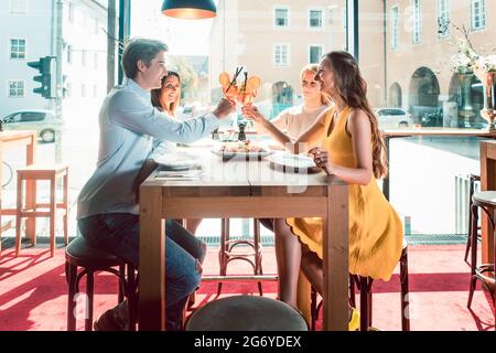 Genießen Sie den Blick auf die Hände von vier jungen Freunden, die mit frischen Orangencocktails toasten, bevor Sie in einem trendigen Restaurant Meeresfrüchte essen Stockfoto