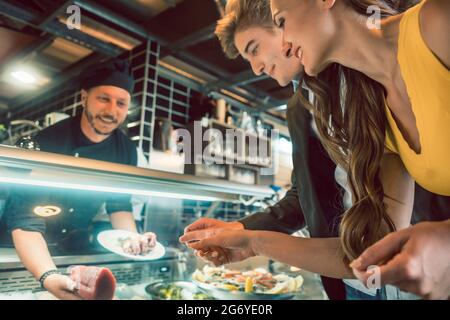 Erfahrene Koch Auswahl rohe Meeresfrüchte aus dem Gefrierschrank für zwei Kunden in einem trendigen Restaurant und Cafeteria mit frischen Lebensmitteln Stockfoto