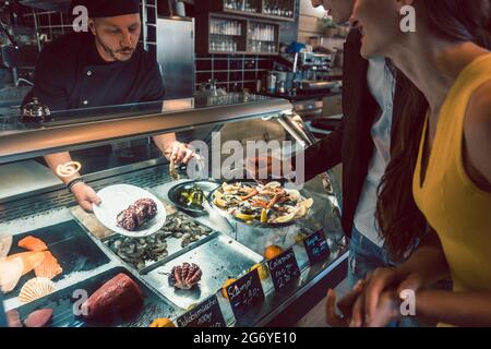 Erfahrene Koch Auswahl rohe Meeresfrüchte aus dem Gefrierschrank für zwei Kunden in einem trendigen Restaurant und Cafeteria mit frischen Lebensmitteln Stockfoto