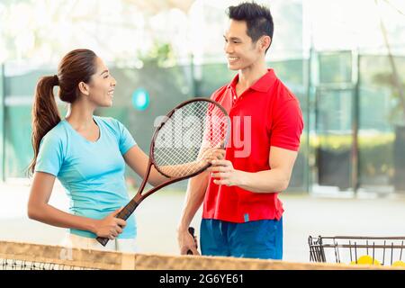 Chinesische Tennislehrer Lächeln beim unterrichten Anfänger weibliche Spieler den richtigen Griff mit dem Schläger als professioneller Spieler Stockfoto