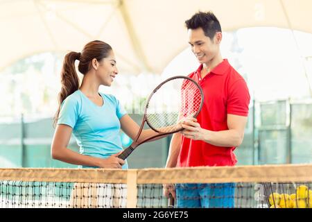 Chinesische Tennislehrer Lächeln beim unterrichten Anfänger weibliche Spieler den richtigen Griff mit dem Schläger als professioneller Spieler Stockfoto