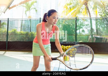 Schöner asiatischer Tennisspieler, der konzentriert nach vorne blickt und dabei den Schläger und den Ball hält, bevor er zu Beginn des Spiels dient Stockfoto