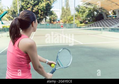 Rückansicht einer jungen Frau mit rosa ärmellosem Oberteil, die auf einem professionellen Tennisplatz in der Stadt Tennis spielt Stockfoto