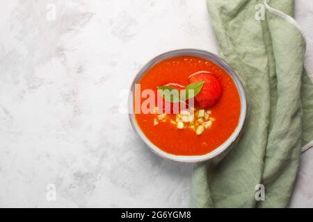 Ein Teller mit kalter Gazpacho-Püree-Suppe. Traditionelles spanisches Gericht mit ausgewogener Tomaten-, Pfeffer- und Tabasco-Sauce auf grauem Betonboden mit Olivenbäumen Stockfoto