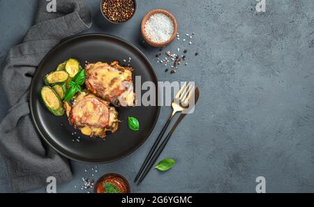 Gebackenes Fleisch mit Pilzen, Tomaten und Käse auf grauem Hintergrund mit Gewürzen und einer Leinenserviette. Stockfoto
