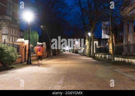 Vor dem New Walk Museum in der Nacht zeigt Frau, die mit Bewegungsunschärfen auf der linken Seite läuft. Zeigt das Museum auf der rechten Seite, mit hellen Straßenlampen. Stockfoto