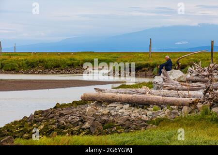 Mann sitzt auf einem großen Felsen mit Blick auf den Ozean vom Garry Point Park in Steveston british Columbia, Kanada Stockfoto