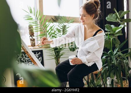 Frau, die auf einem Stuhl vor der Staffelei sitzt und malt Stockfoto