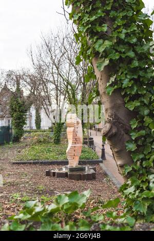 Die Clothier-Skulptur von John Atkin, viele Bäume und Hecken. Großer Baum auf dem Foto mit Efeu, der ihn heranwächst. Zeigt das New Walk Museum im Hintergrund. Stockfoto