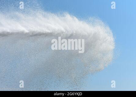 Starker Wasserstrahl aus dem Feuerwehrschlauch des Autos vor dem Hintergrund des blauen Himmels. Stockfoto