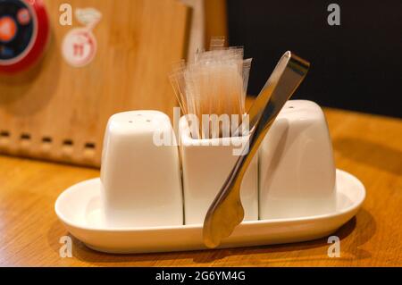 Stellen Sie Porzellansalz, Pfeffer, Zuckerzange, Zahnstocher, rufen Sie den Kellnerknopf auf einen Holztisch Stockfoto