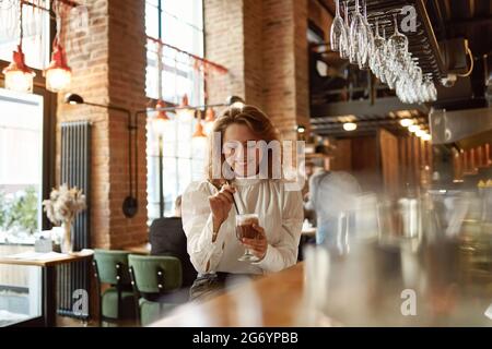 Frau genießt heißen Kaffee, während sie an der Theke sitzt Stockfoto