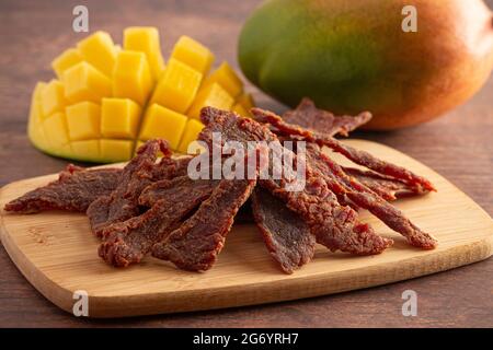 Gourmet Sweet Mango Flavored Beef Jerky auf einem Holzschneidebrettchen Stockfoto