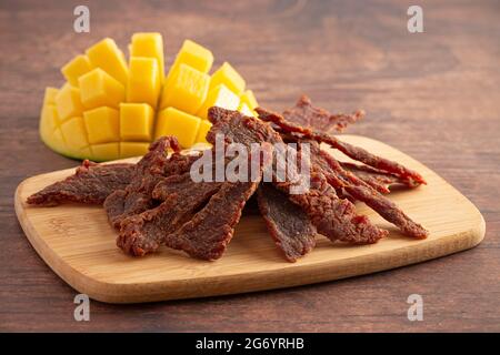 Gourmet Sweet Mango Flavored Beef Jerky auf einem Holzschneidebrettchen Stockfoto