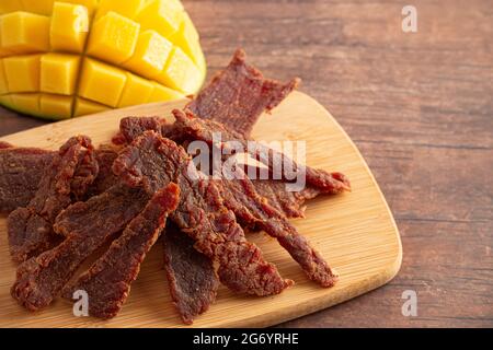 Gourmet Sweet Mango Flavored Beef Jerky auf einem Holzschneidebrettchen Stockfoto