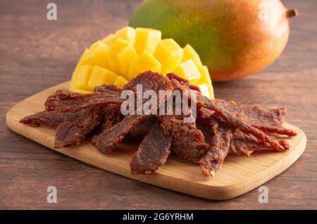 Gourmet Sweet Mango Flavored Beef Jerky auf einem Holzschneidebrettchen Stockfoto