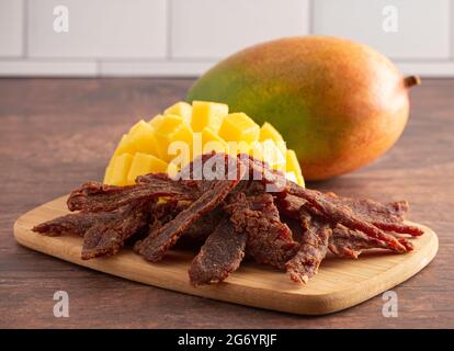 Gourmet Sweet Mango Flavored Beef Jerky auf einem Holzschneidebrettchen Stockfoto