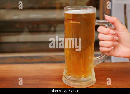 Die Hand einer Frau hält ein Pint gekühltes Bier und setzt es auf einen Holztisch Stockfoto