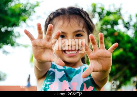 Ein sechsjähriges Mädchen in Peru lächelt und zeigt die Handflächen ihrer Hände mit auseinander gespreizten Fingern. Stockfoto