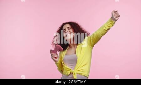 KIEW, UKRAINE - 30. JUNI 2021: Glückliche junge Frau, die Joystick hält und sich isoliert auf Rosa freut Stockfoto