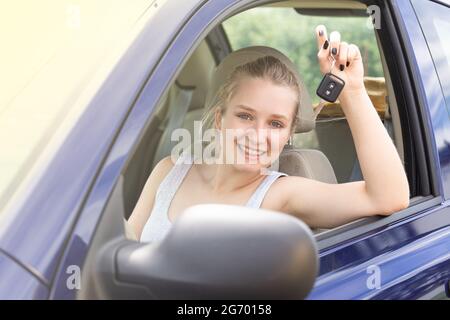 Lächelnde junge Frau auf dem Fahrersitz mit einem Autoschlüssel Stockfoto