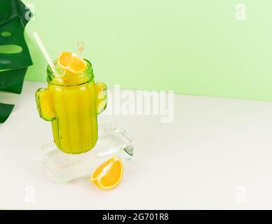 Orangensaft aus kaktusförmigem Glas auf Eisblock mit Fruchtdeko. Speicherplatz kopieren. Stockfoto