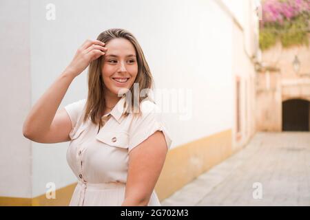 Junge lächelnde Frau genießt den Sommer. Brünett Mädchen in einem beigen Jumpsuit auf den Straßen einer spanischen Stadt. Stockfoto