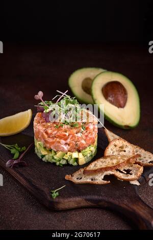 Köstliche Avocado- und gesalzener Lachstartar, serviert mit jungen Kräutern, dunklem Hintergrund, selektiver Fokus Stockfoto