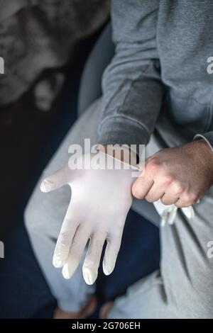 Mann in grauer Kleidung, der medizinische Latexhandschuhe anzt. Das Konzept, Prävention und Schutz vor Coronovirus-Infektion. Stockfoto