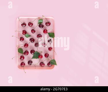 Verkauf von saisonalen, landwirtschaftlichen Beeren, Obst und Gemüse Konzept. Erntezeit. Sommer, Lebensmittelzusammensetzung mit rosa, Kunststoffschale mit natürlichen Kirschen Stockfoto
