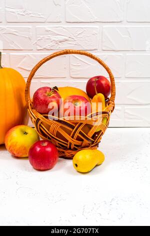 Orangefarbene Kürbisse mit Äpfeln und Birnen in einem Weidenkorb auf weißem Hintergrund. Stillleben im Herbst. Nahaufnahme. Stockfoto