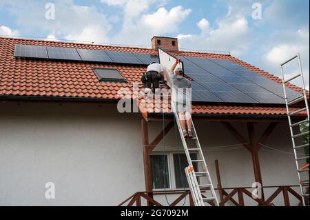 Zwei Ingenieure auf dem Hausdach montieren Photovoltaik-Paneele. Stockfoto