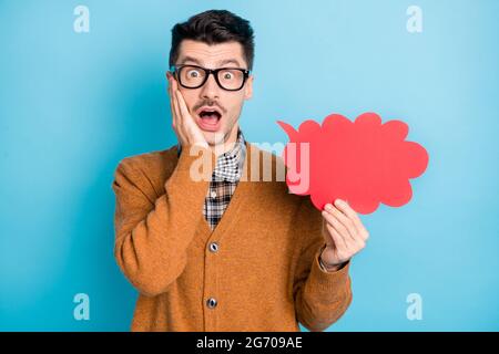 Foto von aufgeregt funky junge Kerl gekleidet braun Cardigan Brille hält rote Wolke Arm Wange isoliert blauen Hintergrund Stockfoto