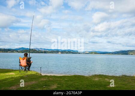 Whakatane New Zealand - Mai 26 2012; Einzelfischer am Ohiwa Harbour Rückansicht geduldig und hoffentlich wartet. Stockfoto