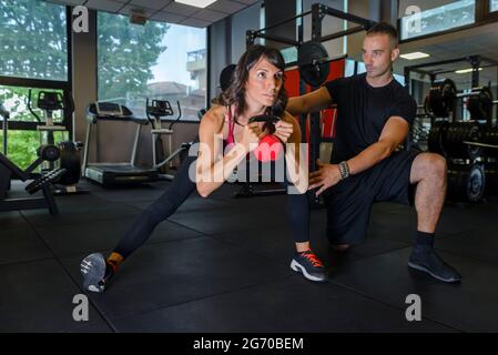 Nahaufnahme einer fokussierten und seriös starken jungen Fitnessfrau in Sportbekleidung, die Liegestütze auf den Kettlebells in der Turnhalle macht, während sie ein persönlicher Trainer ist Stockfoto