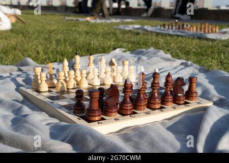 Ein hölzernes Schachbrett mit Figuren in einem Park auf einer grauen Decke. Amateur-Schachturnier im Park auf dem grünen Gras. Stockfoto