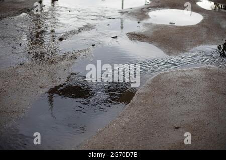 Schmutzige Pfütze auf der Straße. Das Wasser auf der Fahrbahn ablassen. Überflutung der Straße nach dem Regen. Stockfoto