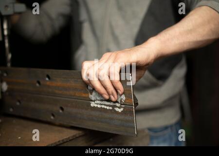 Gebohrte Löcher in das Metall. Arbeiten Sie in einer Metallwerkstatt. Die Hand hält einen Stahlrohling. Ein Mann arbeitet in der Garage. Stockfoto