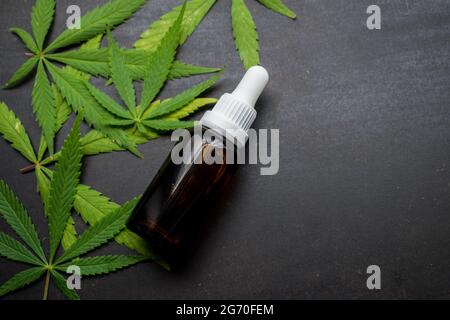 Braune Glasflasche mit Dropper und einigen Cannabisblättern auf einem schwarzen Holztisch mit Platz für Kopien Stockfoto