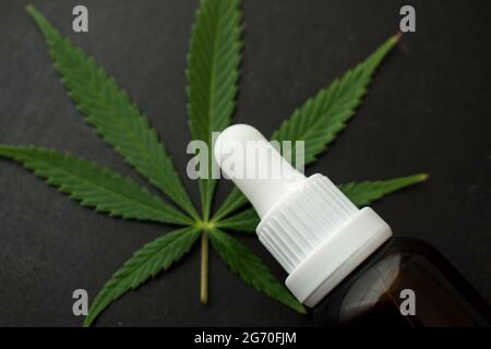 Braune Glasflasche mit Dropper und einigen Cannabisblättern auf einem schwarzen Holztisch mit Platz für Kopien Stockfoto