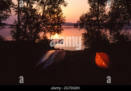 Sonnenaufgang am Ufer des Kawawaymog Lake, Algonquin, Ontario, Kanada, mit zwei umgedrehten Kanus, die einsatzbereit auf dem Boden liegen. Stockfoto