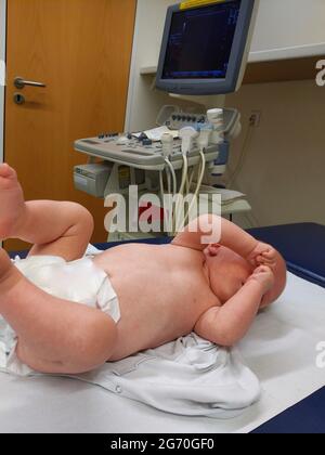 Baby im Ärzteuntersuchungsraum mit Ultraschallscanner im Hintergrund Stockfoto