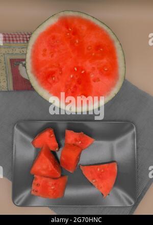 Vertikales Foto von Sommerfrüchten. Rote Wassermelone, die in zwei Hälften und in Stücke geschnitten wurde, zum Essen auf einem Teller serviert, wie von oben gesehen. Stockfoto