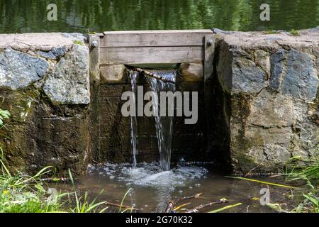 Ein Wasser fließt durch die Schleusen auf dem kleinen Steindamm des Teiches Stockfoto