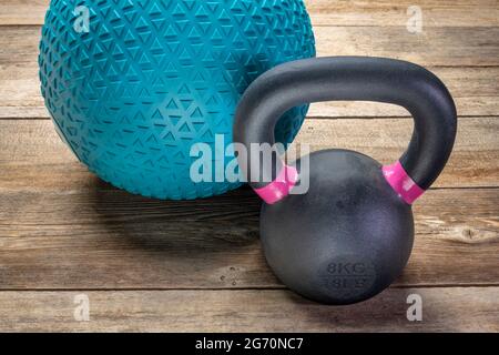 Schwerer, mit Sand und kleiner eiserner Kugelhantel gefüllter Gummiball auf rustikalem Holzhintergrund, Trainings-, Bewegungs- und Fitnesskonzept Stockfoto