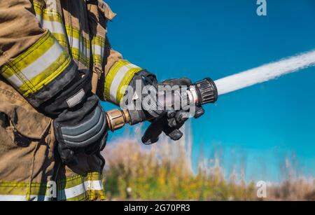 Nahaufnahme der Hände eines Feuerwehranhändes, der einen Schlauch hält und das Hochdruckwasser im Feuer öffnet Stockfoto