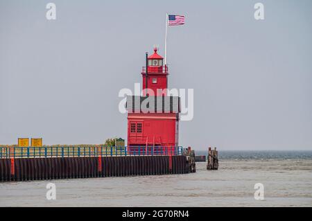 Holland, MI, USA - 8. Juni 2008: Nahaufnahme des Leuchtturms des roten Hafens am dunkelblauen Michigan Lake, wo sich der graue Macatawa See unter hellblauem Himmel leert. Stockfoto