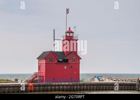 Holland, MI, USA - 8. Juni 2008: Nahaufnahme des Leuchtturms des roten Hafens am Landende mit blauem Michigan Lake unter hellblauem Himmel. Amerikanische Flagge an der Spitze. Stockfoto